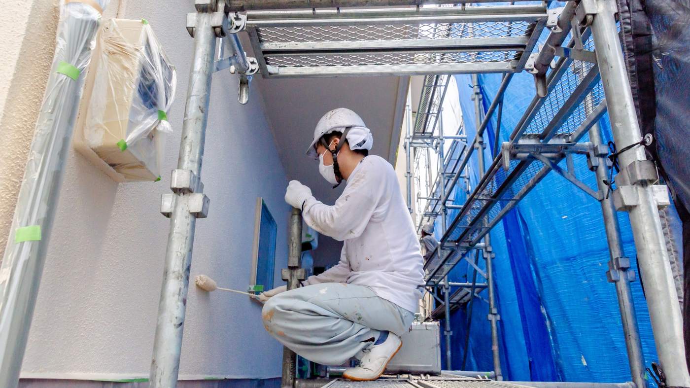 住宅に組まれた足場の上で外壁を塗装する様子