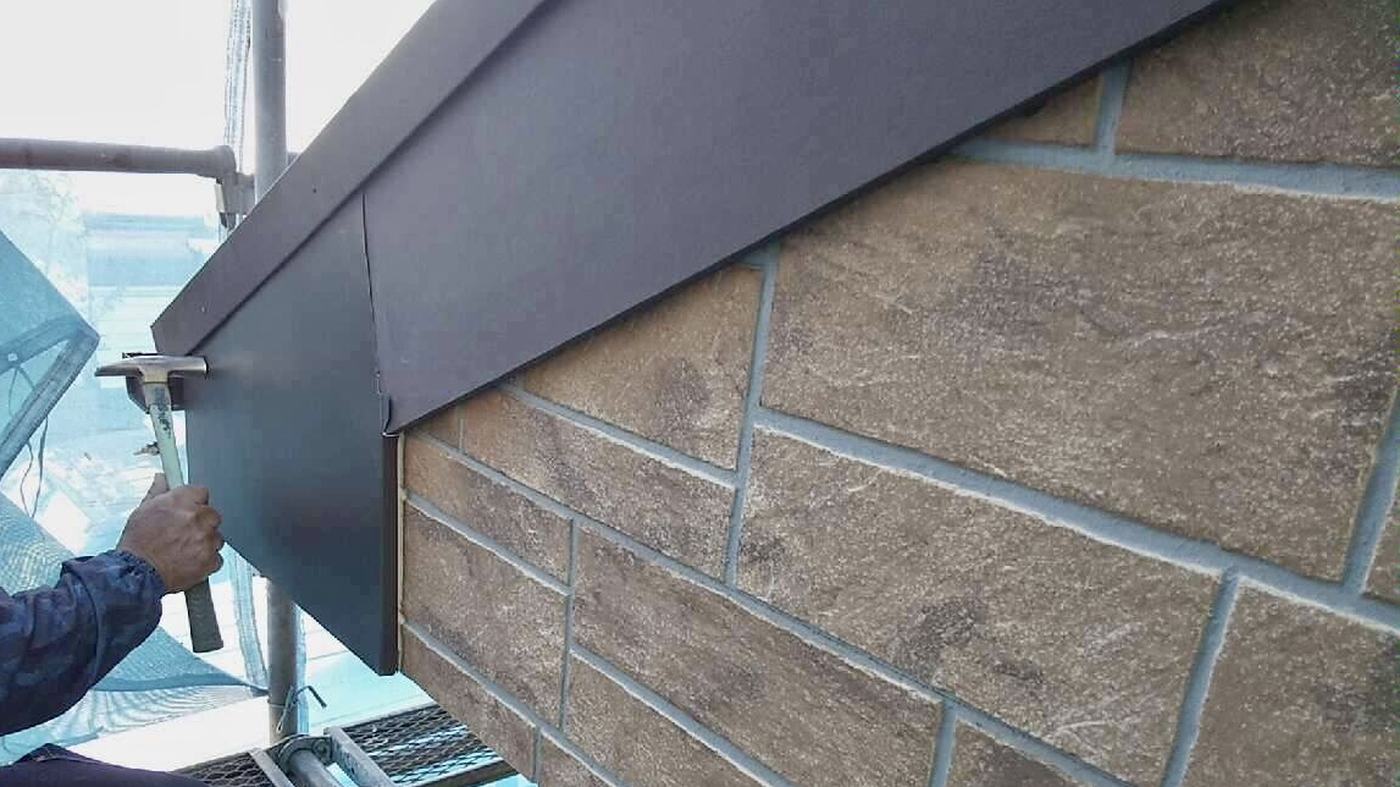 足場の上で屋根の軒先に板金を取り付けている職人