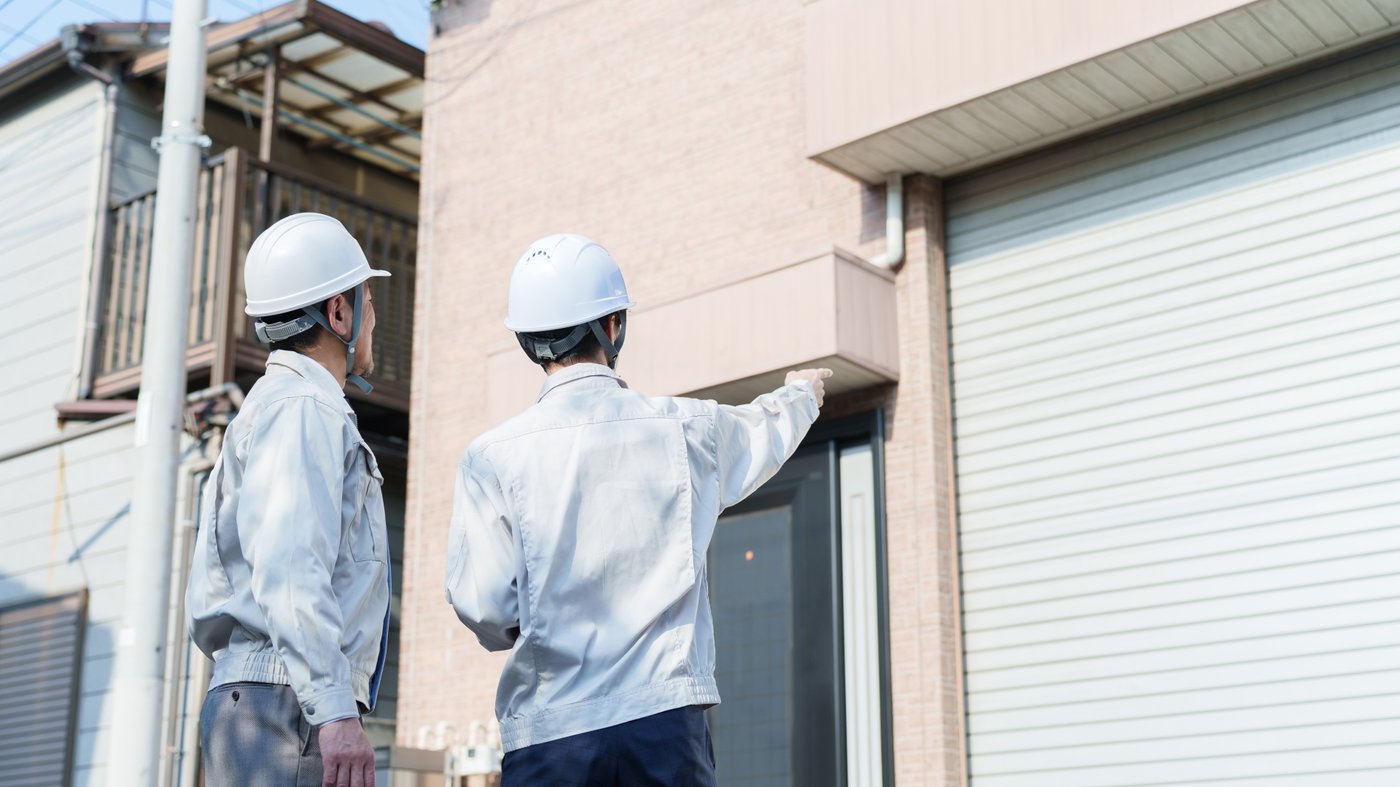 家の外壁を指さして傷み具合を確かめる作業員